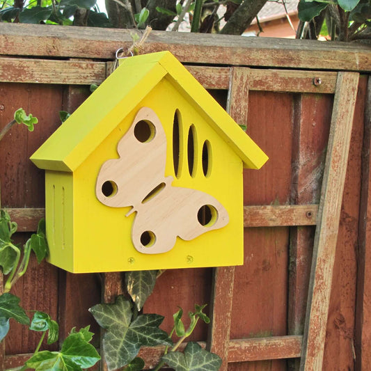 Yellow house-shaped Butterfly House, with a wooden butterfly decoration on the front. 